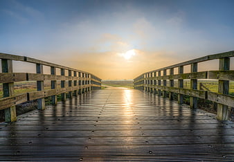 Wooden boardwalk bridge leading to sunrise over wetlands