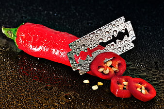 Red Chili Pepper With Razor Blade And Water Droplets On Dark Surface