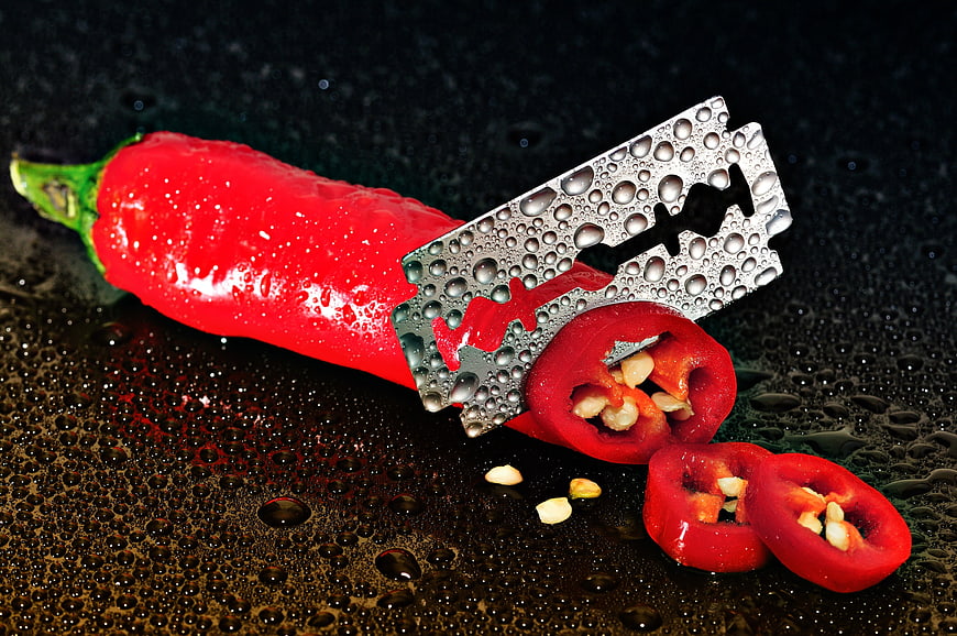 Red Chili Pepper With Razor Blade And Water Droplets On Dark Surface