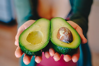 Fresh avocado halves held in hands with pit and green flesh