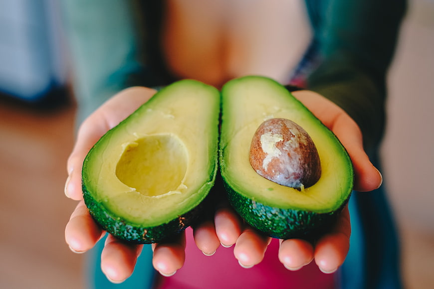 Fresh avocado halves held in hands with pit and green flesh