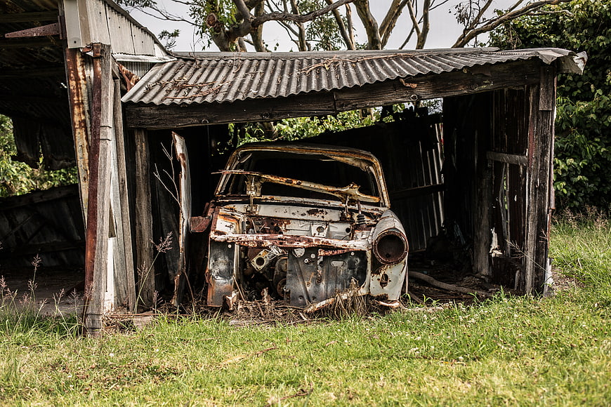 Rusty vintage car wreck in dilapidated wooden shed