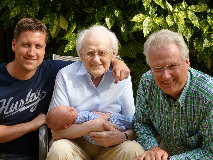 Four Generations Of Men Holding Newborn Baby In Garden