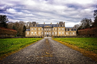 Historic French Manor House With Gravel Driveway And Dramatic Cloudy Sky