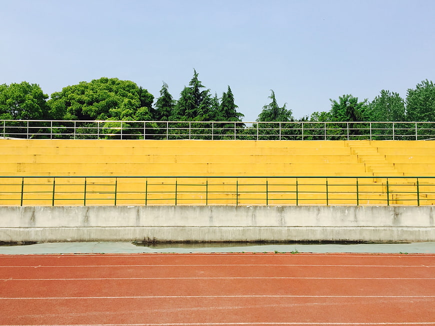 Empty Yellow Stadium Grandstand With Red Running Track And Trees