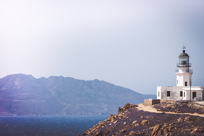 White Lighthouse on Rocky Coastline with Mountain View