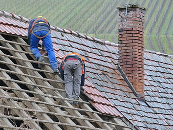 Two workers removing old tiles from a dilapidated roof structure