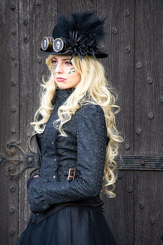 Blonde woman in gothic steampunk costume with skull goggles and feathered hat