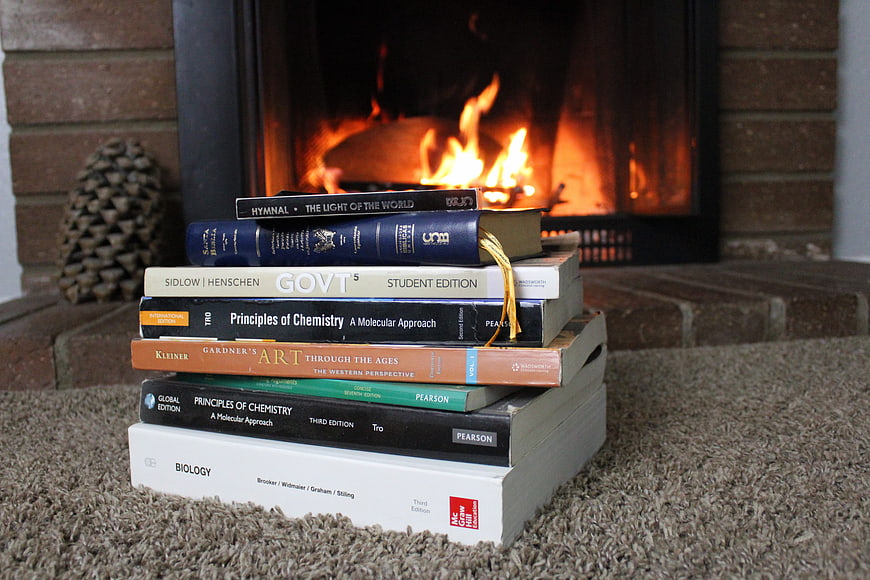 Stack of textbooks and hymnal on carpet in front of a burning fireplace