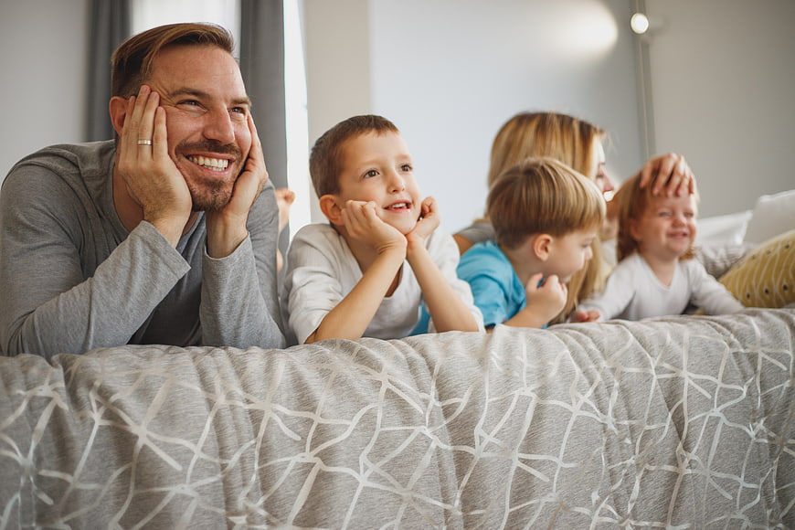 Happy family lying on bed watching TV together