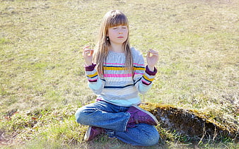 Young girl meditating in a grassy field outdoors