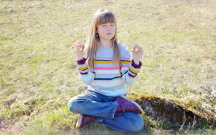 Young girl meditating in a grassy field outdoors