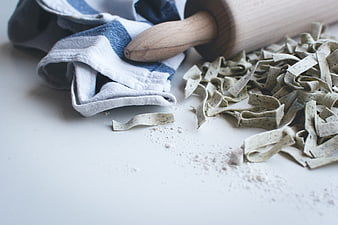 Fresh handmade pasta with rolling pin and flour on white surface