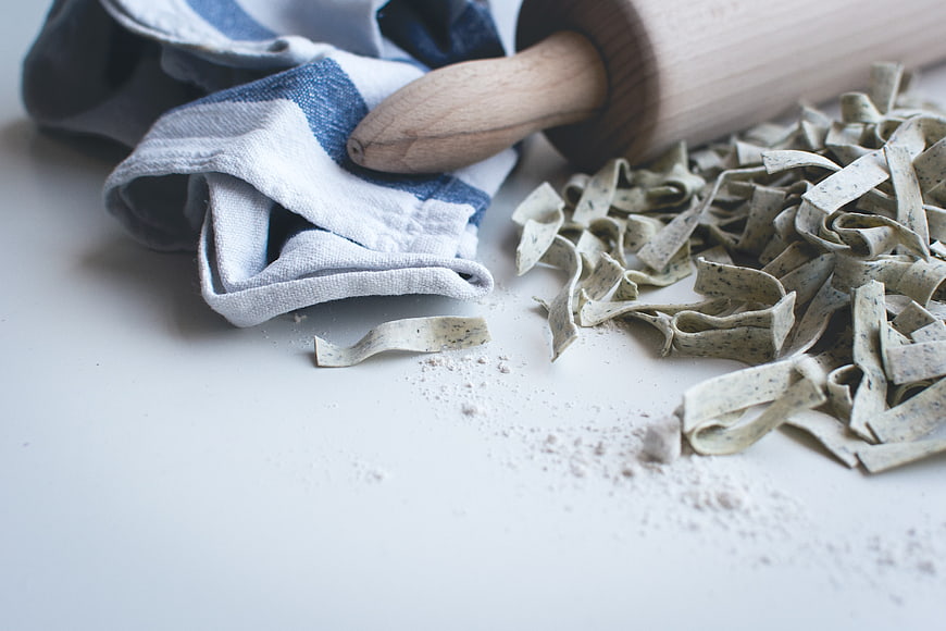 Fresh handmade pasta with rolling pin and flour on white surface