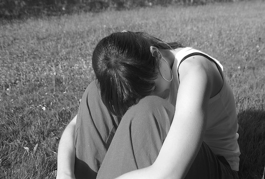 Sad woman sitting alone in grass with head down