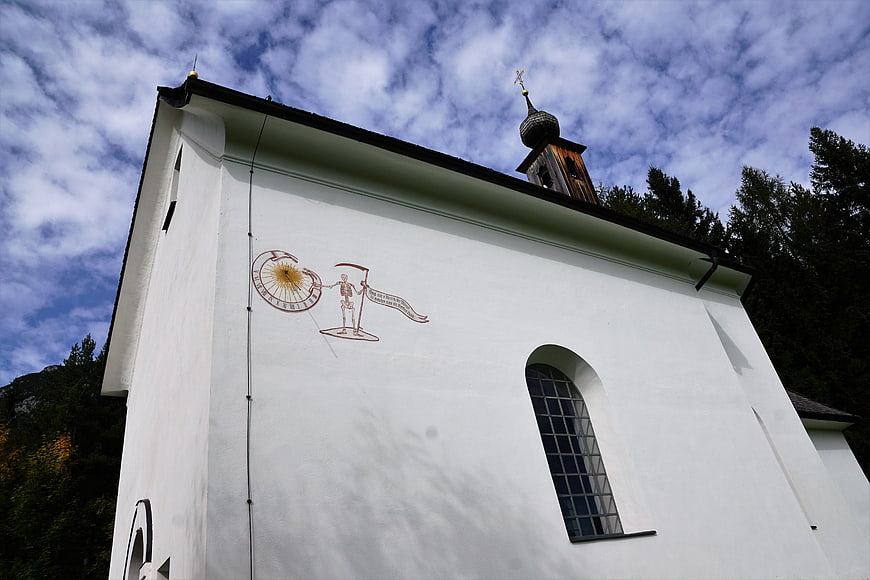 White chapel with skeleton mural and onion dome against cloudy sky