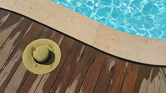 Straw sun hat on wooden deck by swimming pool