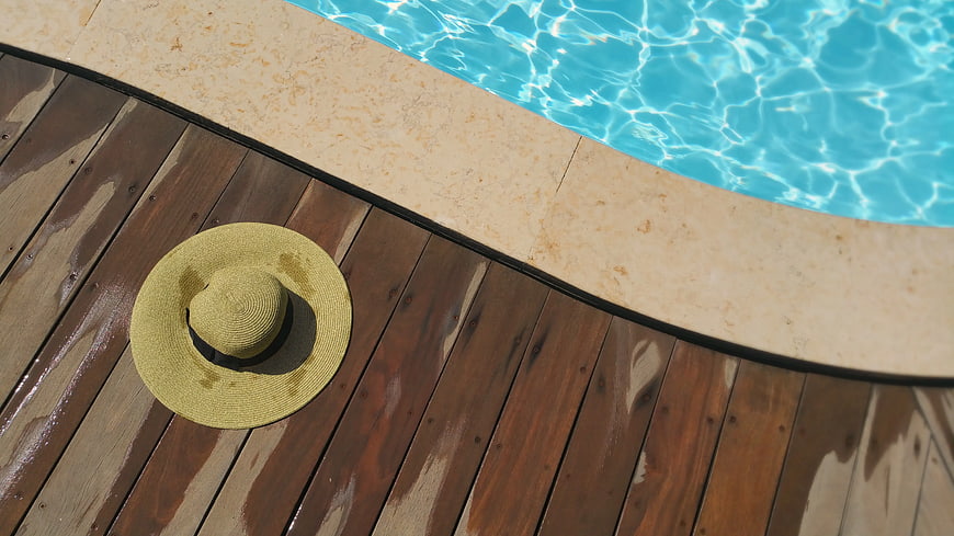 Straw sun hat on wooden deck by swimming pool