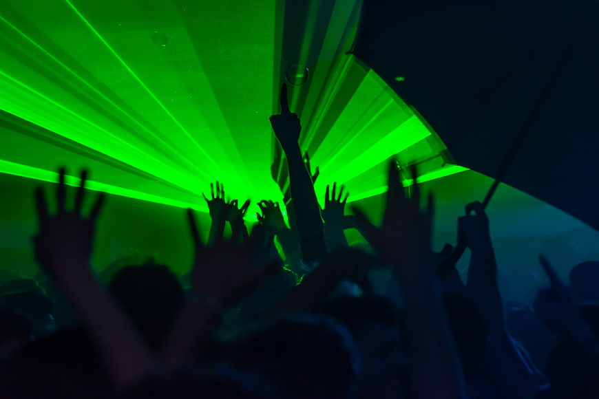 Silhouetted crowd with raised hands under green laser lights at a nightclub