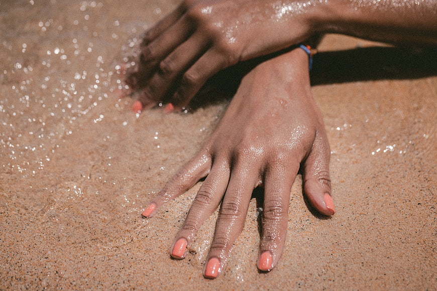 Close-up of hands touching wet sand on a sunny beach