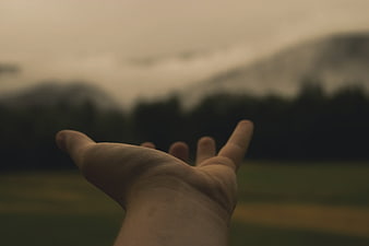 Outstretched hand reaching toward misty mountain landscape