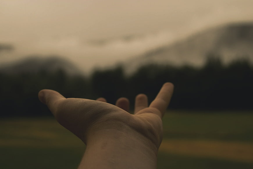 Outstretched hand reaching toward misty mountain landscape