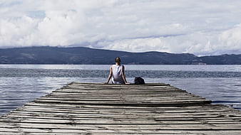Woman sitting alone on wooden pier looking at lake