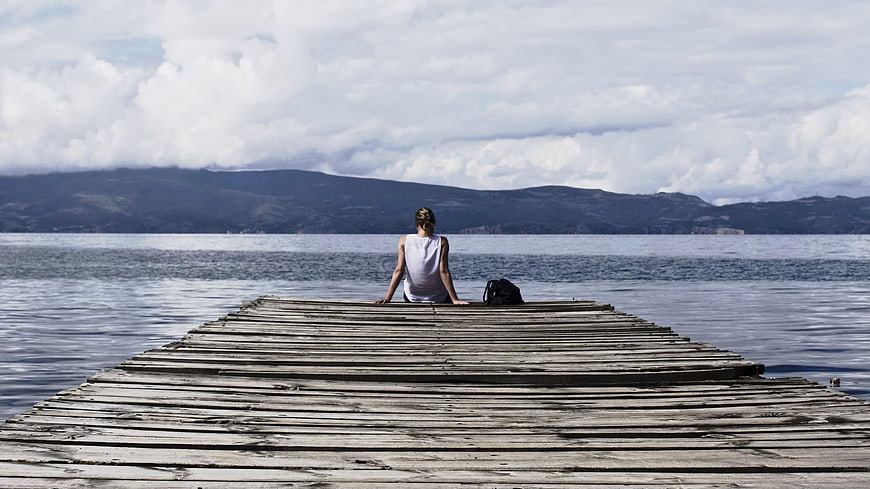 Woman sitting alone on wooden pier looking at lake