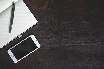 White Smartphone and Notebook on Dark Wood Desk
