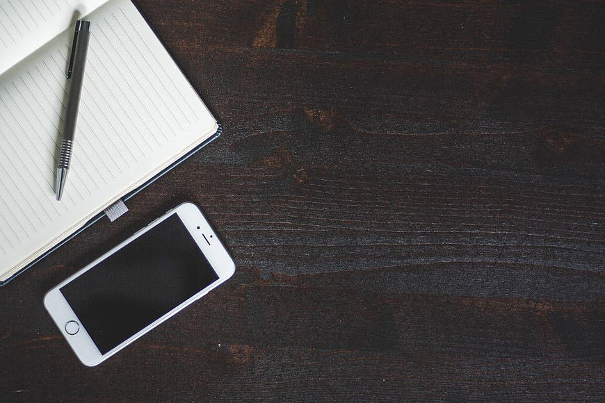 White Smartphone and Notebook on Dark Wood Desk
