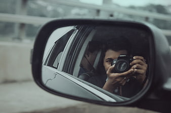 Man taking photo in car side mirror reflection