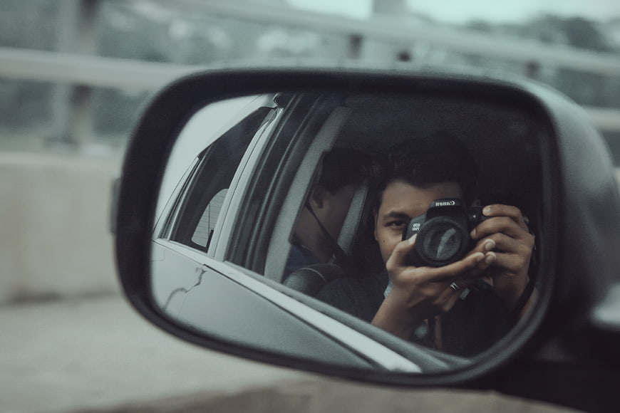 Man taking photo in car side mirror reflection