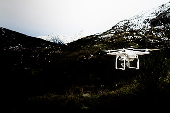 White drone flying over dark mountain landscape with snow