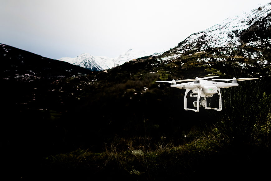White drone flying over dark mountain landscape with snow