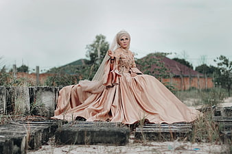Woman in Elegant Peach Wedding Gown Sitting on Concrete Blocks