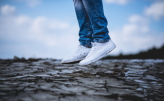 Low angle of white sneakers jumping over cracked dry earth