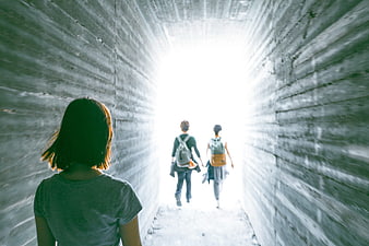 People Walking Through Concrete Tunnel Toward Bright Light