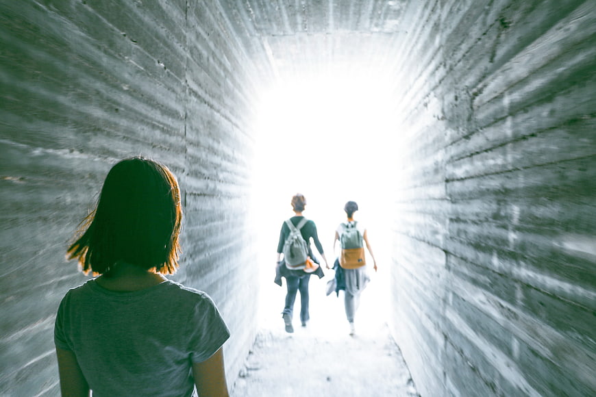 People Walking Through Concrete Tunnel Toward Bright Light