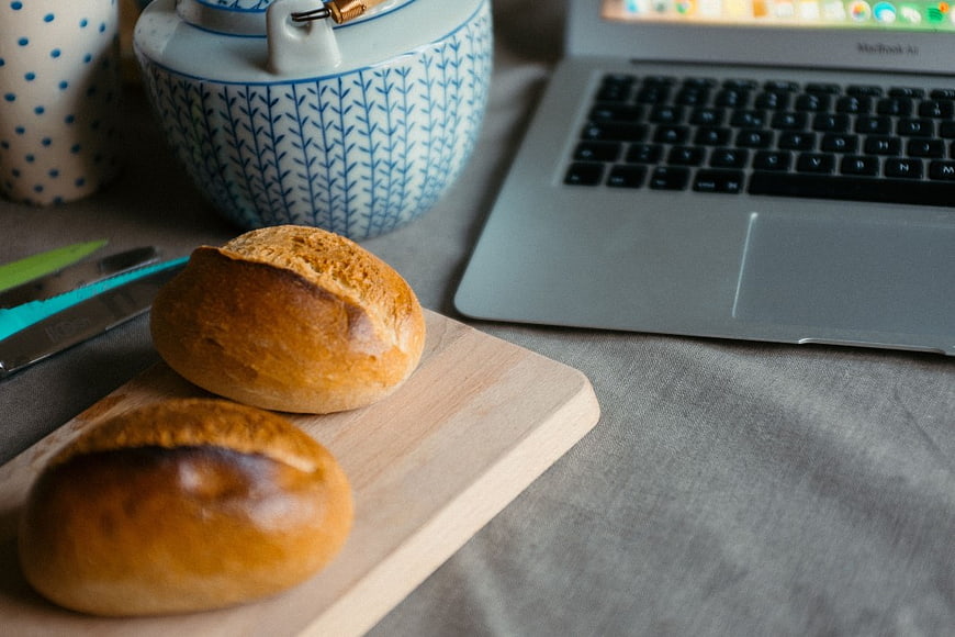 Fresh Bread Rolls on Wooden Board with Laptop