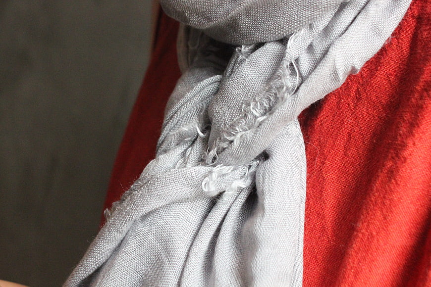 Close-up of gray frayed scarf on red sweater