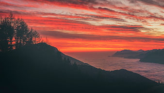 Dramatic red sunset over mountain peaks and sea of clouds