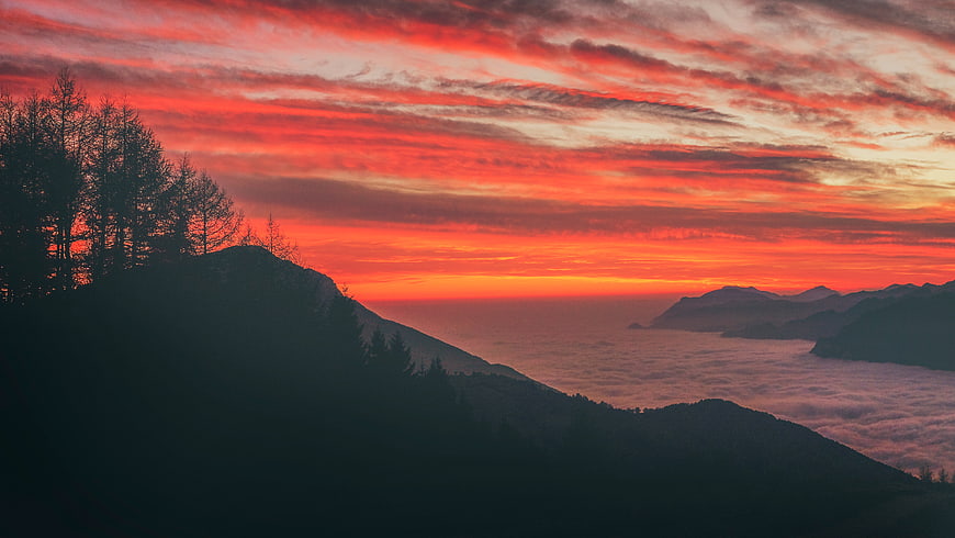 Dramatic red sunset over mountain peaks and sea of clouds