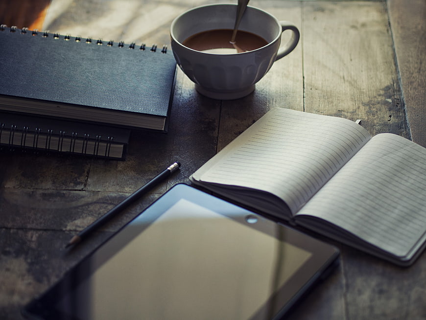 Workspace with coffee, notebooks, and tablet on wooden table