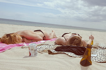 Two women relaxing on beach towels with drinks