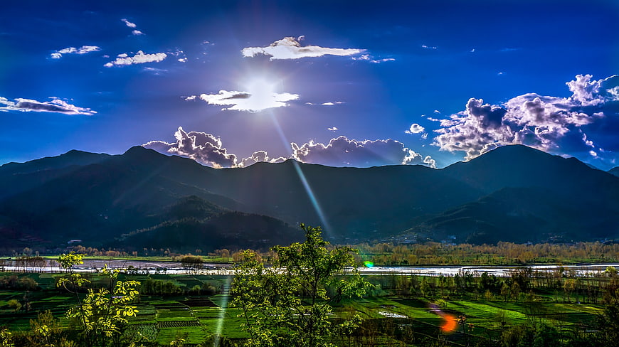 Sunlit Mountain Valley with River and Green Fields