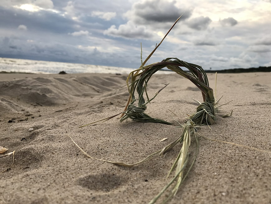 Braided reed ring on sandy beach with cloudy sky