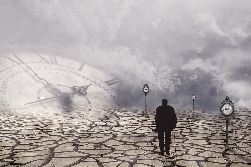 Silhouette of elderly man walking on cracked earth with clocks