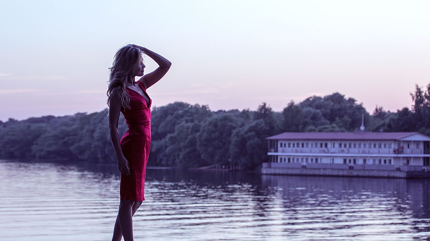 Woman in red dress standing by a river at dusk
