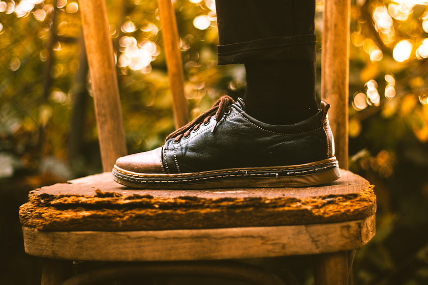 Black leather shoe on rustic wooden chair in autumn forest