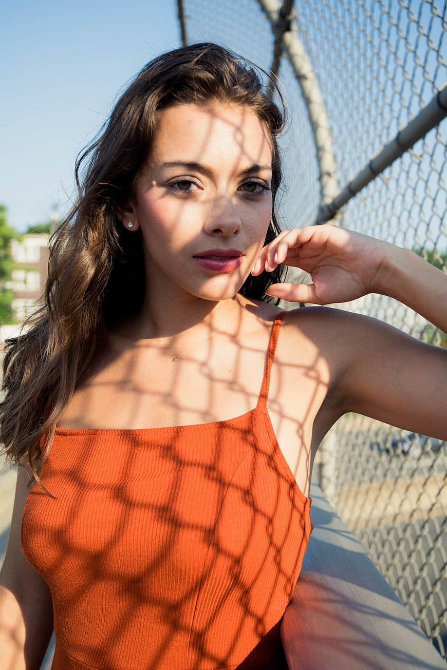 Woman in Orange Top with Chain Link Fence Shadows